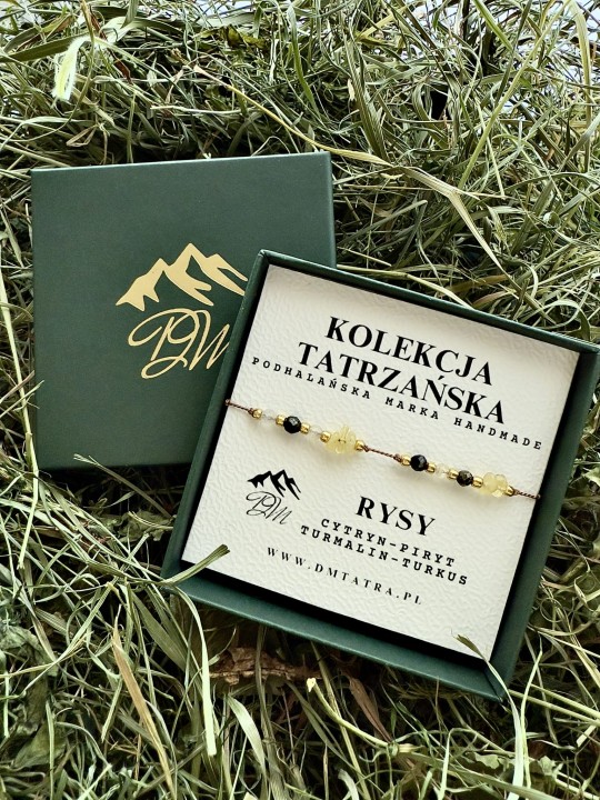 Bransoletka Rysy z Kolekcji Tatrzańskiej DM Tatra, wykonana z cytrynu, pirytu, turmalinu i turkusu, prezentowana w zielonym pudełku na tle suszonej trawy; obok drugie pudełko z logo marki, w naturalnej, górskiej aranżacji.