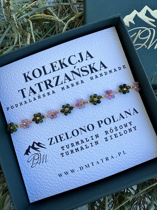 Delikatna bransoletka Zielono Polana z drobnymi turmalinami zielonymi i różowymi w kwiatowych splotach, ułożona w zielonym pudełku DM Tatra, w naturalnej aranżacji z suszonymi trawami.